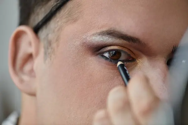 A queer person applies eyeliner to their eye with precision, creating a striking look. — Stock Photo