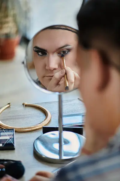 A queer person applies makeup in front of a mirror. — Stock Photo