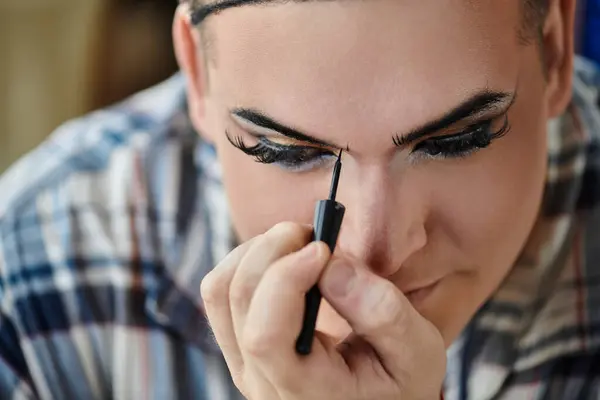 A queer person applies eyeliner with focused concentration. — Stock Photo
