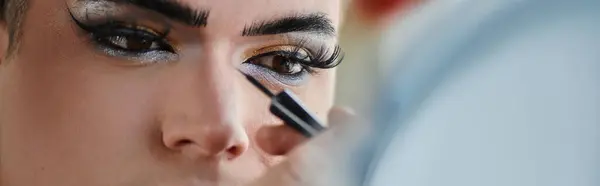 A queer person has their eye makeup applied with a black eyeliner. — Stock Photo