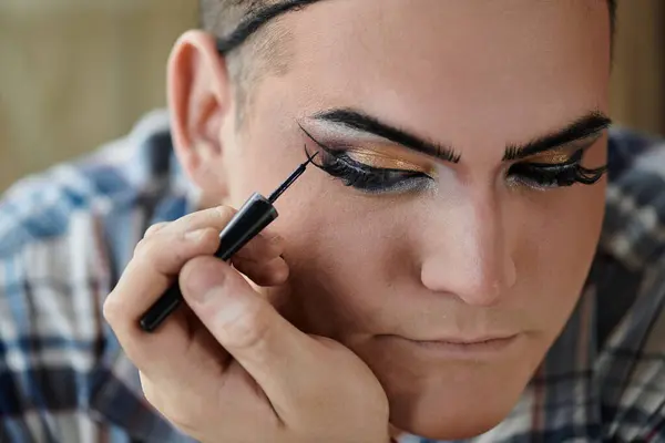A queer person applies eyeliner with a focused expression, creating a bold look. — Stock Photo