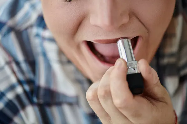 A close-up shot of a queer person applying lipstick, a hint of color adding to their confident smile. — Stock Photo