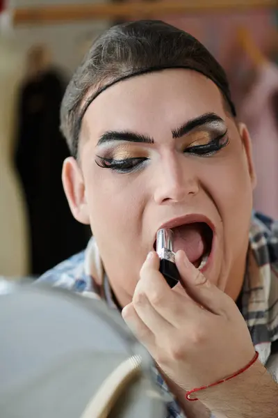 A queer person applies lipstick, looking directly at the camera with a confident smile. — Stock Photo
