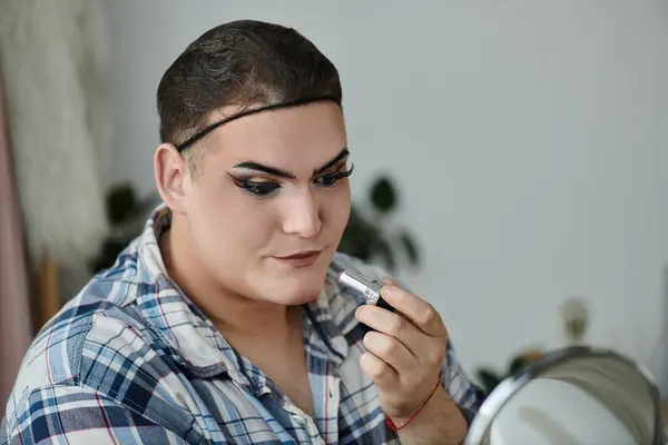 A queer person applies makeup in a stylish plaid shirt, showcasing their unique sense of self. — Stock Photo