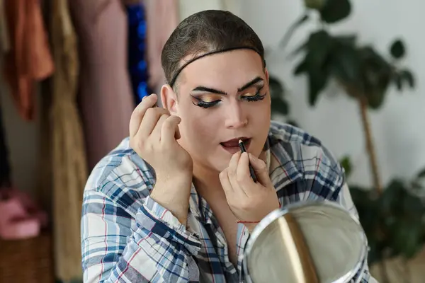 A queer person in stylish attire applies lip liner while looking in a mirror. — Stock Photo