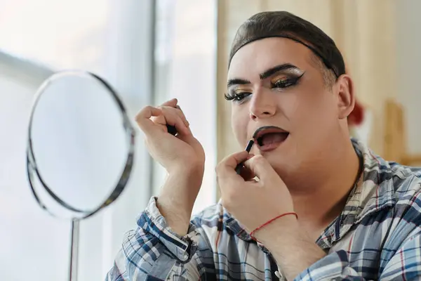 A queer person applies lip liner while looking in the mirror. — Stock Photo