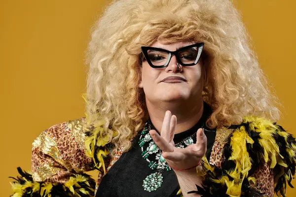 A queer person in a glamorous outfit poses against a yellow background. — Stock Photo