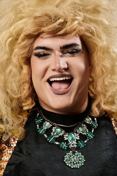 A smiling queer person with blonde hair and a glamorous green necklace. — Stock Photo
