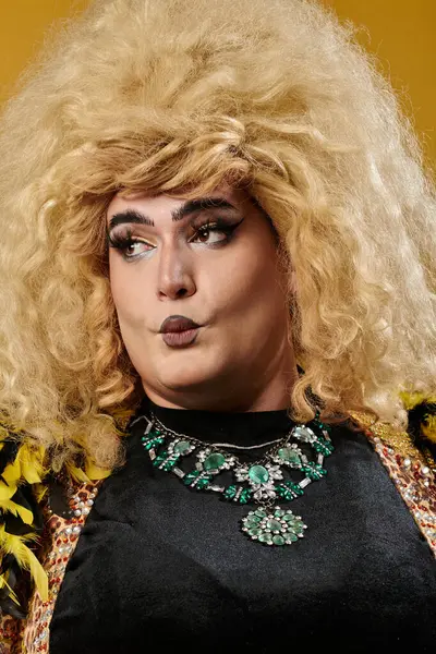 A queer person with a large blonde wig and elaborate jewelry looks intently to the side. — Stock Photo
