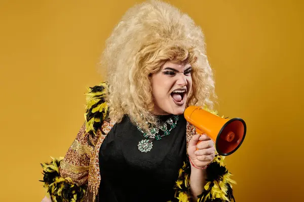 A queer person in a vibrant yellow outfit shouts into a megaphone. — Stock Photo