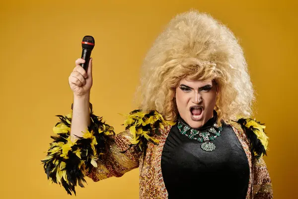 Una drag queen in un abito glamour e una grande parrucca bionda canta in un microfono. — Foto stock