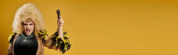 A drag queen dressed in a gold jacket and feathers holds a microphone. — Stock Photo