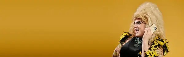 A glamorous individual with a big smile holds a phone in a bright yellow studio. — Stock Photo