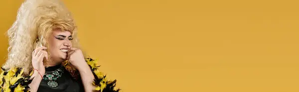 A drag queen in a yellow feathered jacket smiles against a bright yellow backdrop. — Stock Photo
