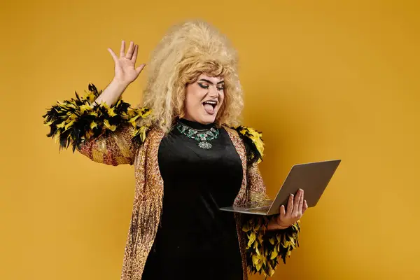 Eine Drag Queen im stylischen Outfit winkt mit einem Laptop in die Kamera. — Stockfoto