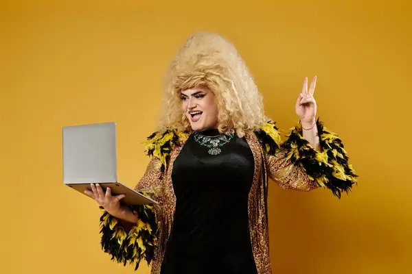 A drag queen wearing a fashionable outfit holds a laptop and flashes a peace sign. — Stock Photo