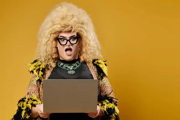 Uma drag queen em uma roupa elegante e peruca grande reage a algo em seu laptop. — Fotografia de Stock
