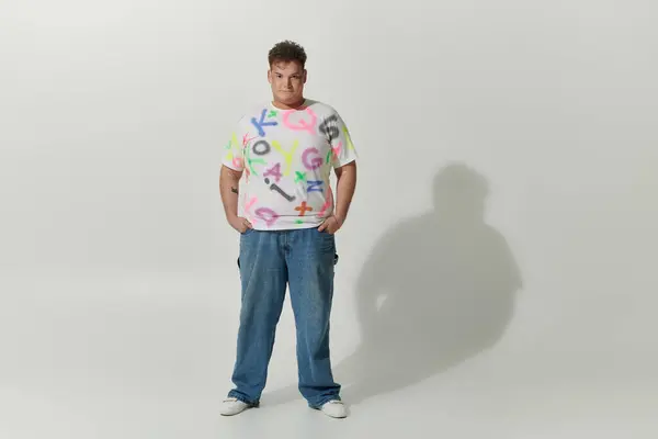 Queer person in graffiti-style white tee poses against white background — Stock Photo
