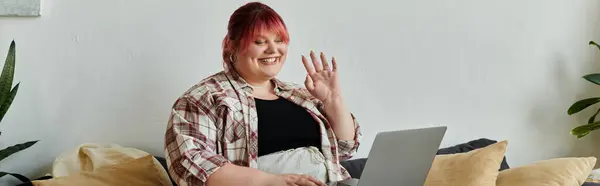Un plus size donna sorride e le onde ciao mentre seduto su un divano. — Foto stock