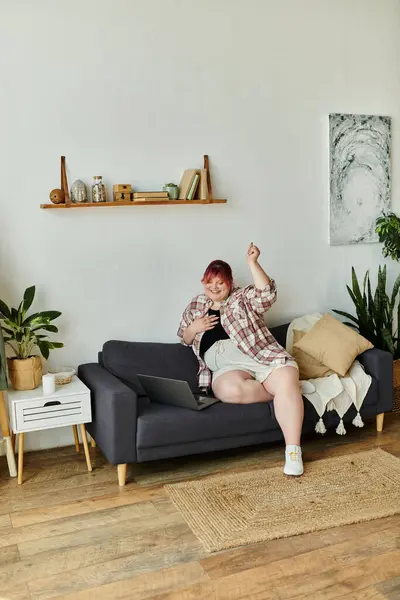 Eine Frau entspannt sich auf einer Couch, lächelt und hebt zur Feier die Hand. — Stockfoto