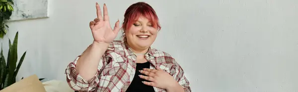 Женщина plus-size с розовыми волосами ярко улыбается, сидя в помещении. — стоковое фото