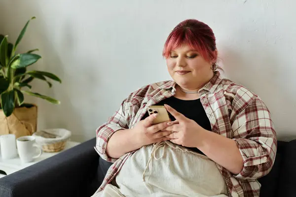 A woman in a plaid shirt relaxes on a couch while scrolling on her phone. — Stock Photo