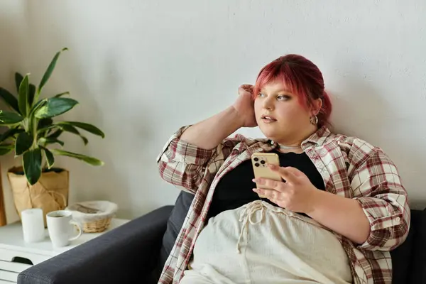 A woman with pink hair relaxes on a couch, holding a phone. — Stock Photo