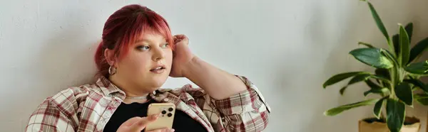 Uma mulher com cabelo rosa relaxa em sua casa, percorrendo cuidadosamente seu telefone. — Fotografia de Stock