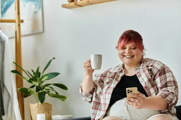 Eine Plus-Size-Frau lächelt, während sie an ihrem Kaffee nippt und durch ihr Handy blättert. — Stockfoto