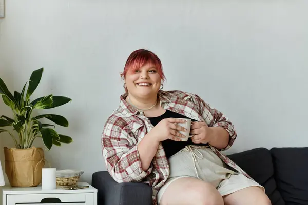 Una mujer sonríe cálidamente mientras disfruta de una taza de café en su sofá. — Stock Photo