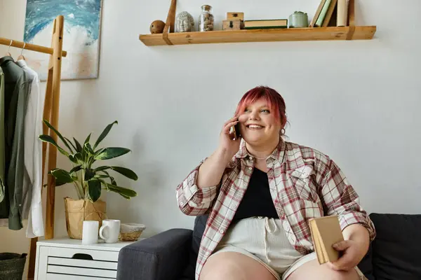 Eine Frau im karierten Hemd sitzt zu Hause auf einer Couch und telefoniert mit einem Lächeln. — Stockfoto