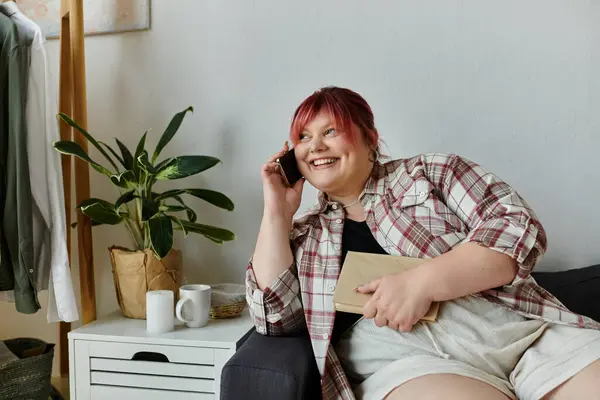 Una mujer de talla grande disfruta de una llamada telefónica mientras está sentada en un sofá. - foto de stock