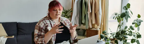 A woman wearing a plaid shirt gestures while sitting at a table at home. — Stock Photo