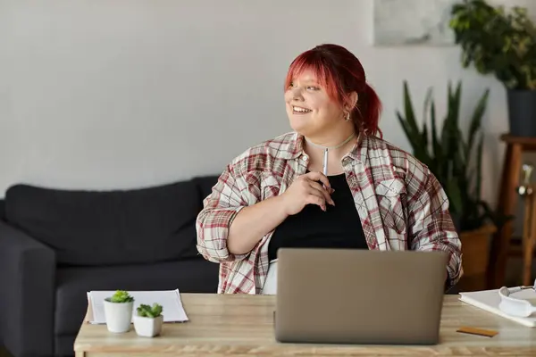 A woman sits at her desk, thoughtfully holding a pen, with a laptop in front of her. — Stock Photo