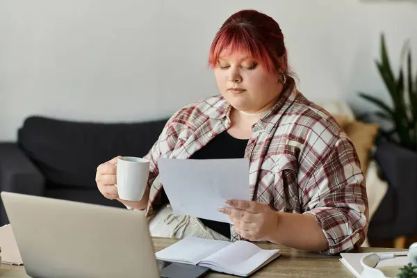 Eine Frau sitzt an ihrem Schreibtisch und liest bei einer Tasse Kaffee ein Dokument. — Stockfoto