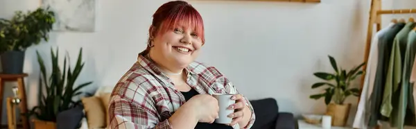 Eine Frau lächelt freundlich, hält einen Becher in der Hand und genießt einen ruhigen Moment zu Hause. — Stockfoto