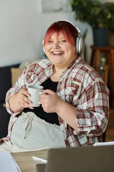 A woman smiles brightly as she enjoys a cup of coffee while wearing headphones at home. — Stock Photo