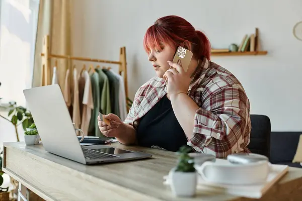 Una donna con i capelli rossi usa il suo telefono e un computer portatile per fare acquisti online da casa. — Foto stock