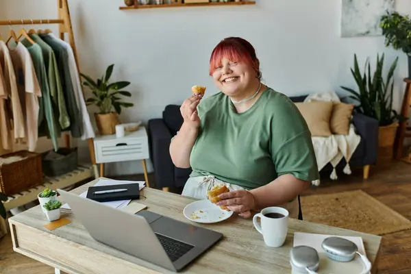 A plus-size woman enjoys a snack and coffee while working from home. — Stock Photo