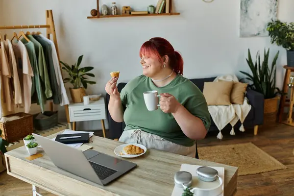 Uma mulher se senta em uma mesa com um laptop, café e uma pastelaria, sorrindo. — Stock Photo