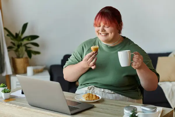 A plus-size woman enjoys a pastry and coffee while working from home. — Stock Photo