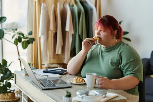 Donna dai capelli rossi mangia pasticceria, beve caffè, con computer portatile aperto — Foto stock