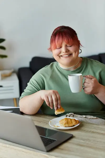 Una donna si gode una pausa caffè a casa, assaporando un croissant e un momento di pace. — Foto stock