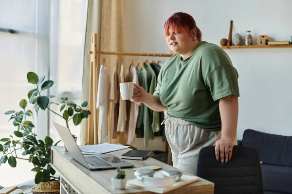 A woman stands near a desk, holding a cup of coffee and looking relaxed. — Stock Photo