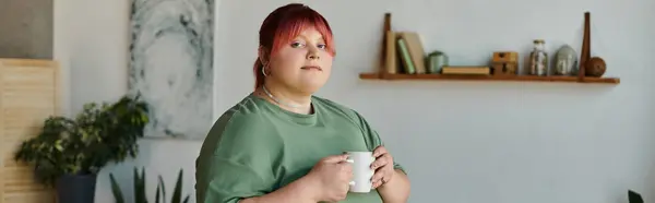 Женщина plus size с розовыми волосами держит кружку в гостиной. — стоковое фото