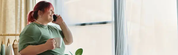 A smiling woman talks on the phone while holding a cup, enjoying a sunny day at home. — Stock Photo