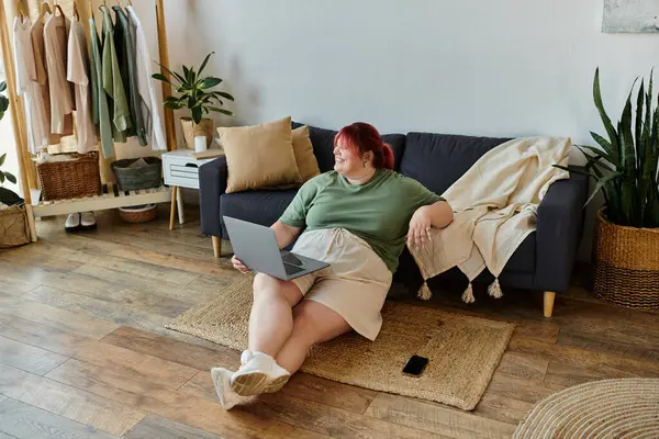 A woman sits on the floor, using a laptop while smiling. — Stock Photo