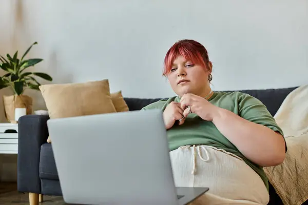 A woman sits on a couch, looking intently at a laptop in her lap. — Stock Photo