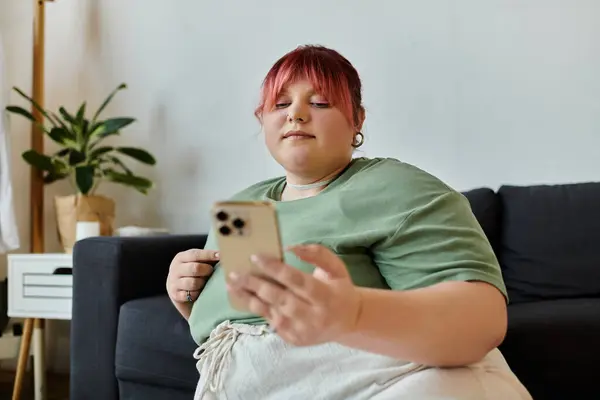 Uma mulher com uma camisa verde senta-se em um sofá, rolando pelo telefone. — Fotografia de Stock