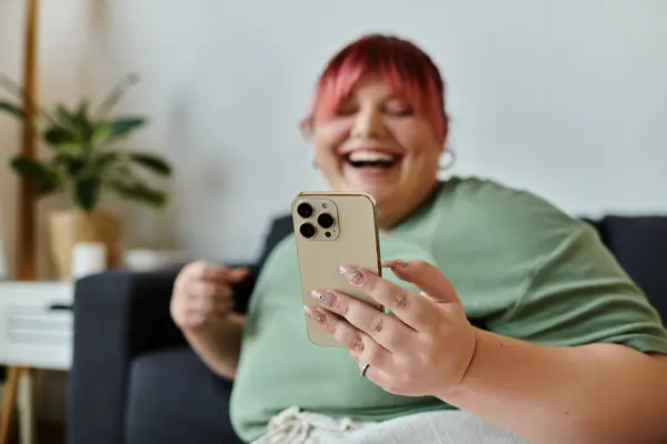 Женщина plus size сидит на диване, смеется и смотрит на смартфон. — стоковое фото